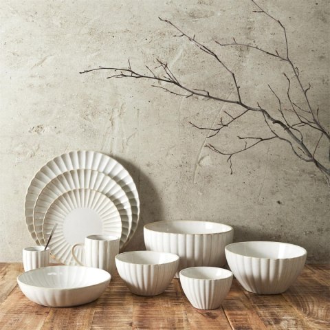Zestaw beżowych naczyń ceramicznych z kolekcji Beju, w tym talerze i miska Beju Boru III pod betonową ścianą.