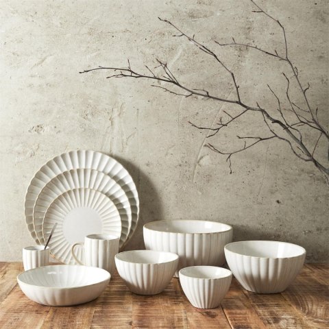 Kolekcja beżowych naczyń ceramicznych Beju Sara II z misami i talerzami na tle surowej ściany.