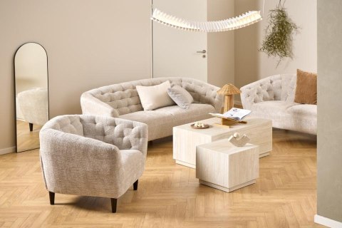 Elegancki beżowy fotel japandi Gofun w pikowanej tkaninie ustawiony w salonie obok nowoczesnej sofy i białego stolika.